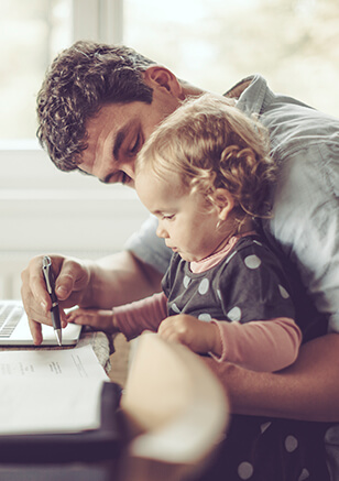 man holding his daughter while he works on the computer