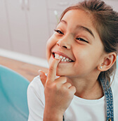 young girl pointing at her bright, white teeth